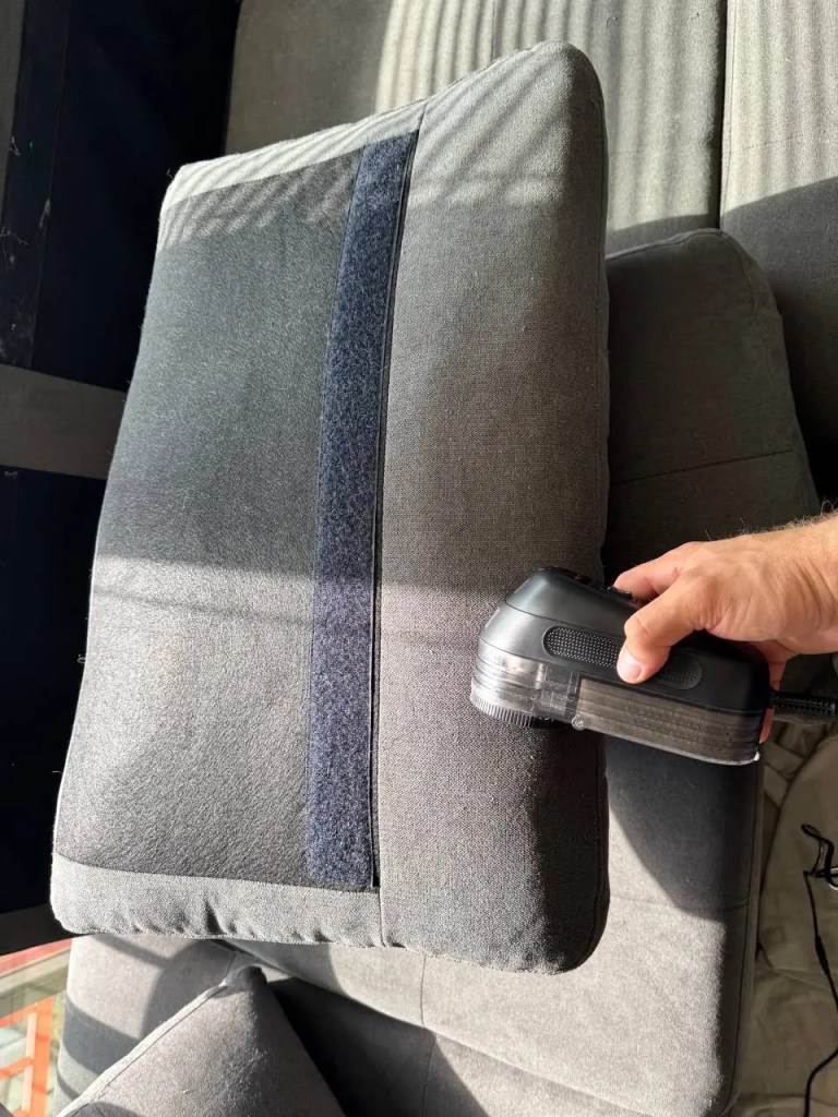 Fabric shaver removing lint from gray upholstered sofa
