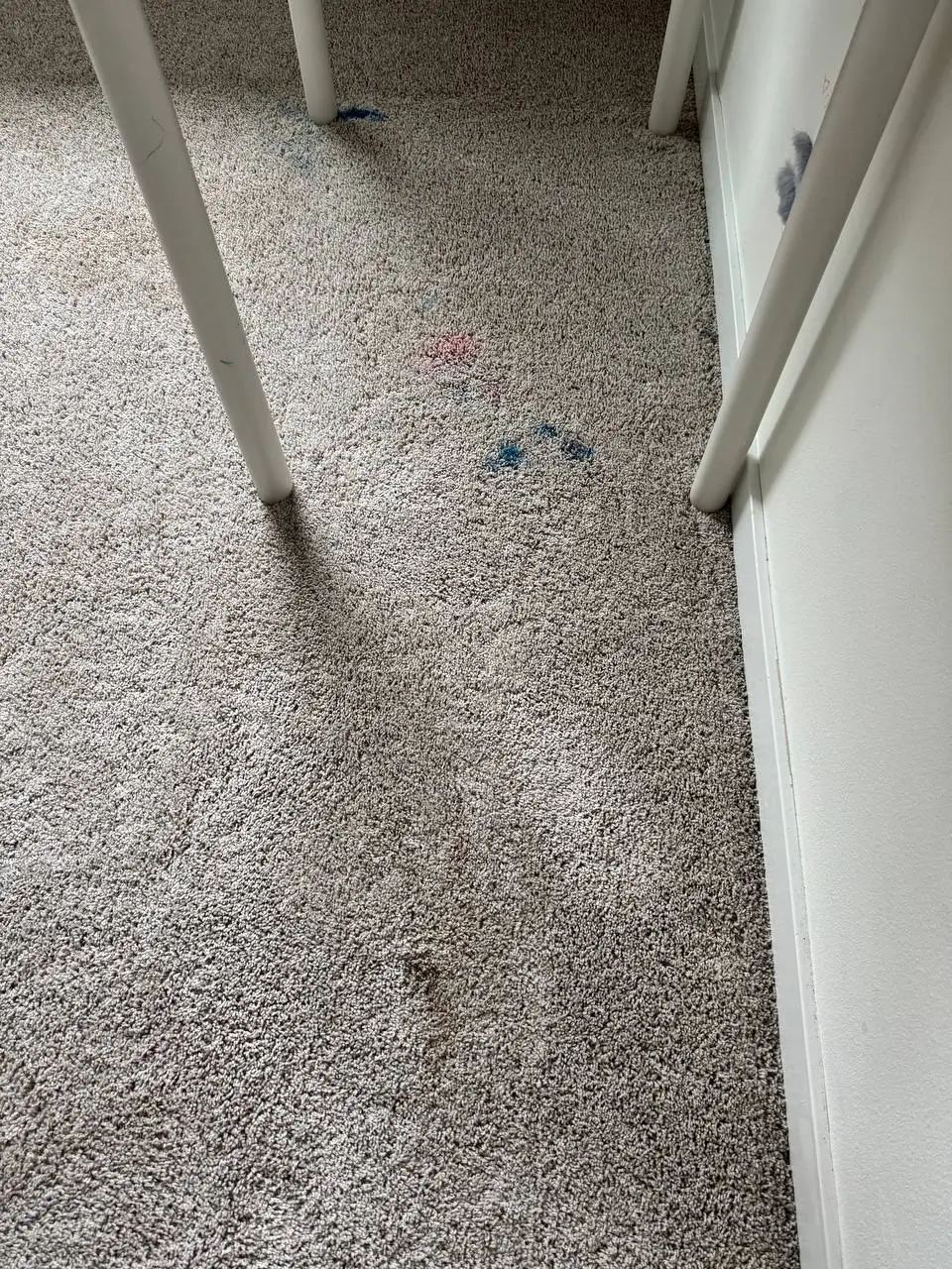 Red and blue paint stains visible on carpet beneath white furniture before treatment